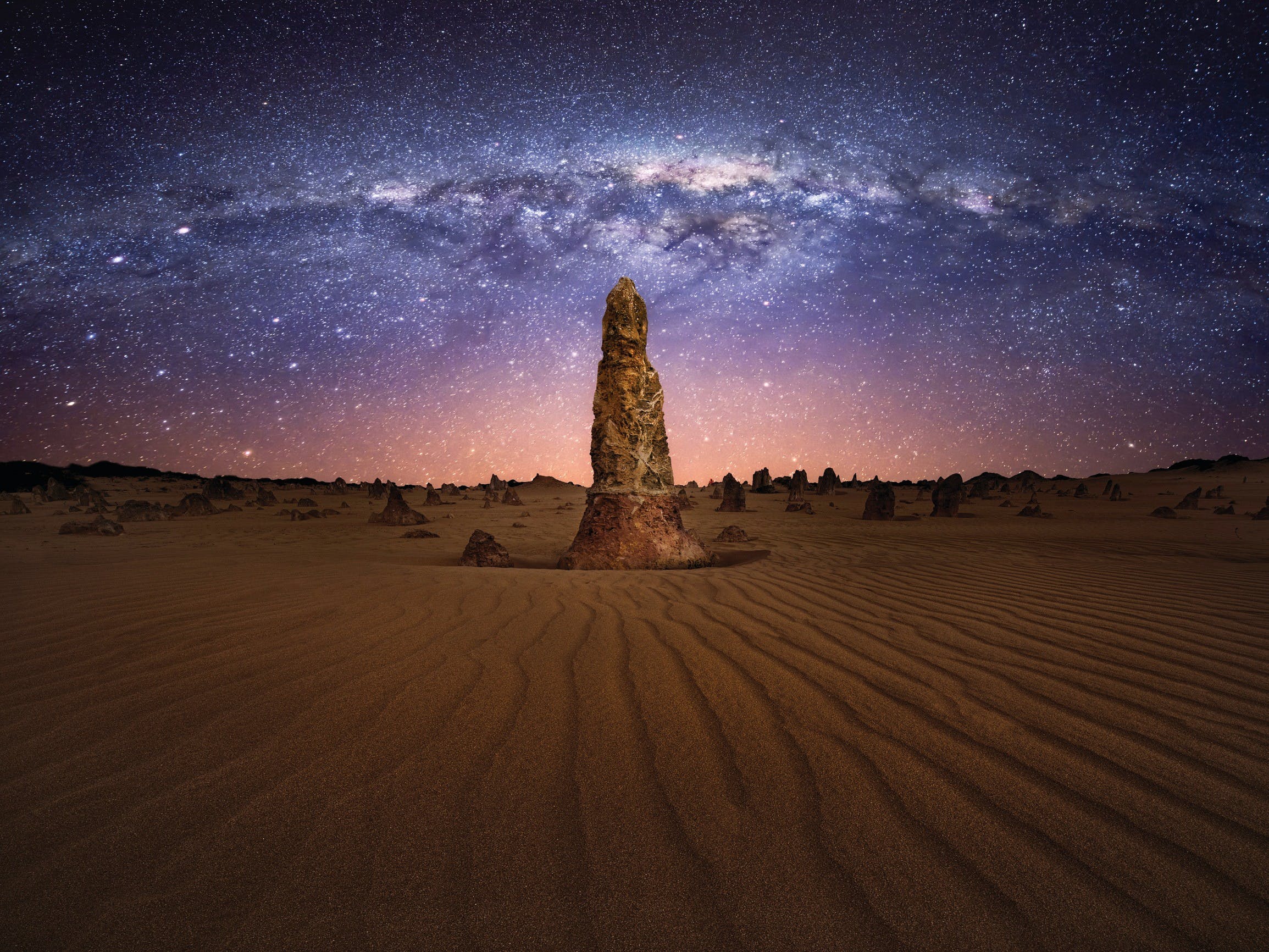 single pinnacle rock formation under a starry night sky