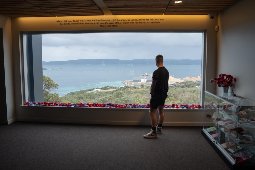 A person looking out a large window with a coastline view