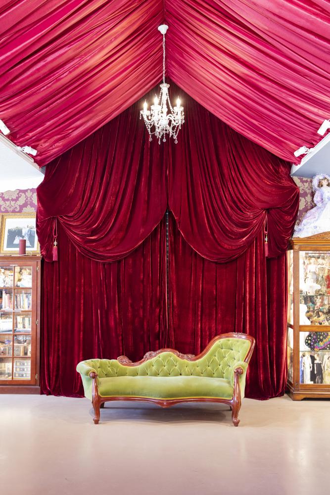 A room with red velvet curtains and a velvet green chaise lounge