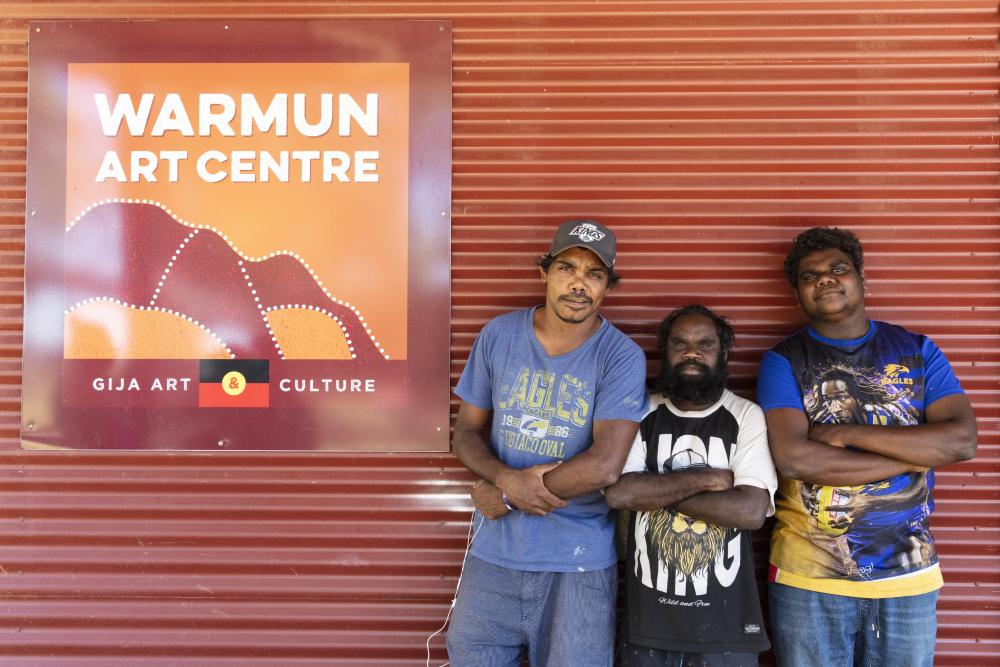 Three people standing next to a sign for the Warum Art Centre
