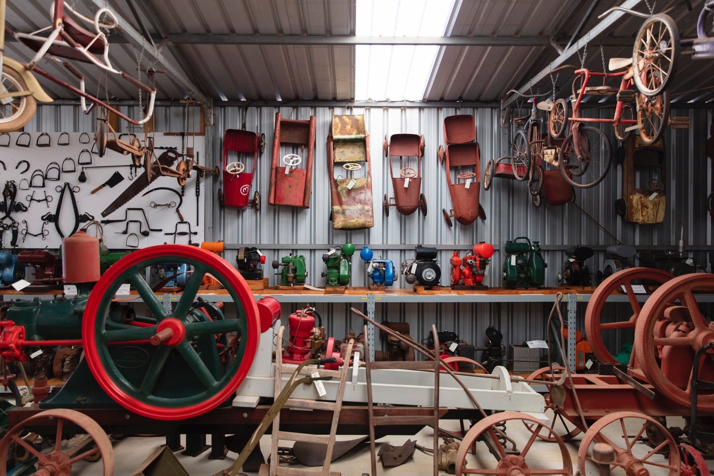 A shed with vintage farm equipment, bicycles and toy cars on display.