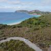 Aerial view of a car on a road winding through bushland with a beach and ocean in the distance